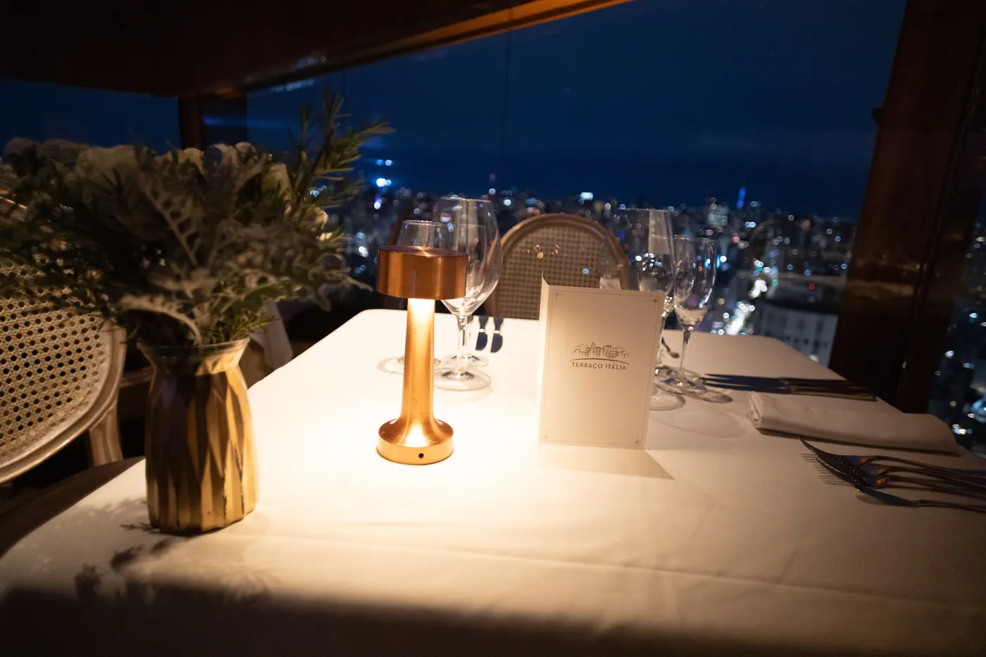 Gedeckter Tisch im Licht einer Tischlampe, dahinter die Lichter von São Paulo