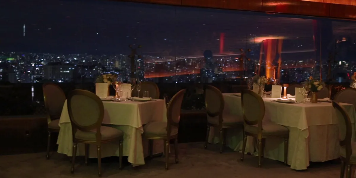 Die Sala Nobre des Terraço Itália am Abend, mit gedeckten Tischen vor den Fenstern und der erleuchteten Stadt draußen