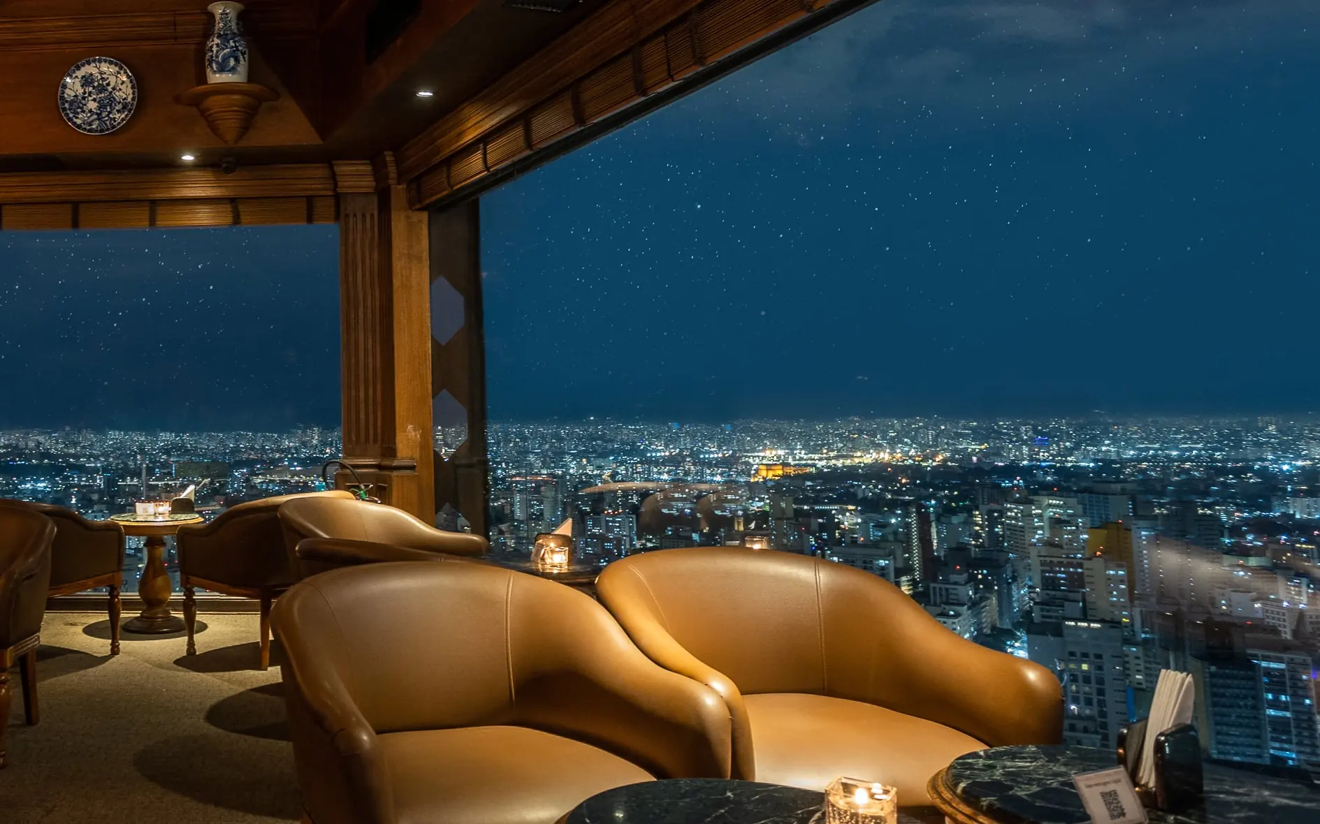 Ledersessel in der Lounge des Terraço Itália vor den Fenstern, dahinter das bis zum Horizont erleuchtete São Paulo